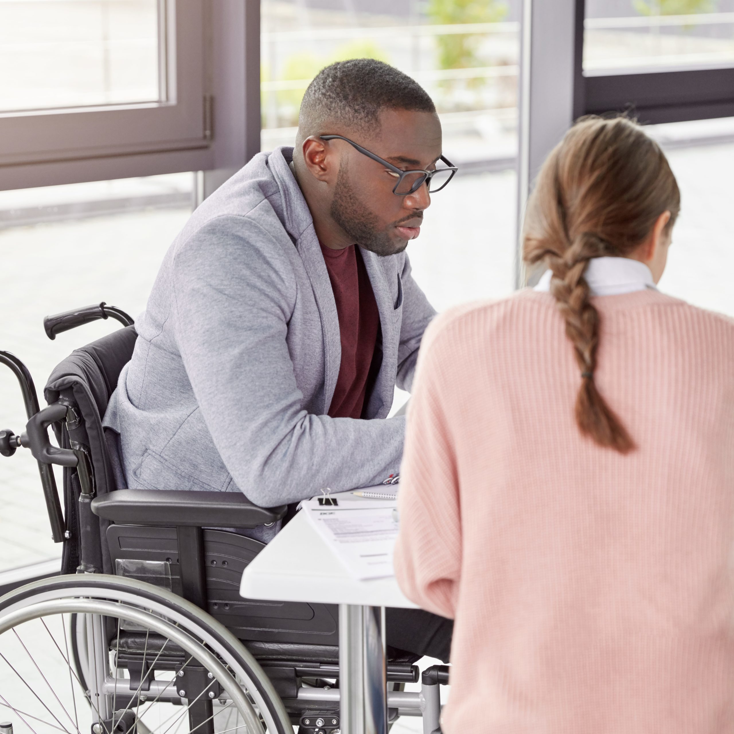 man in a wheelchair sat at a table talking to a female colleague